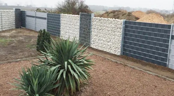 Zaun aus mit Steinen gefülltem Drahtgitter hinter frisch angelegtem Blumenbeet